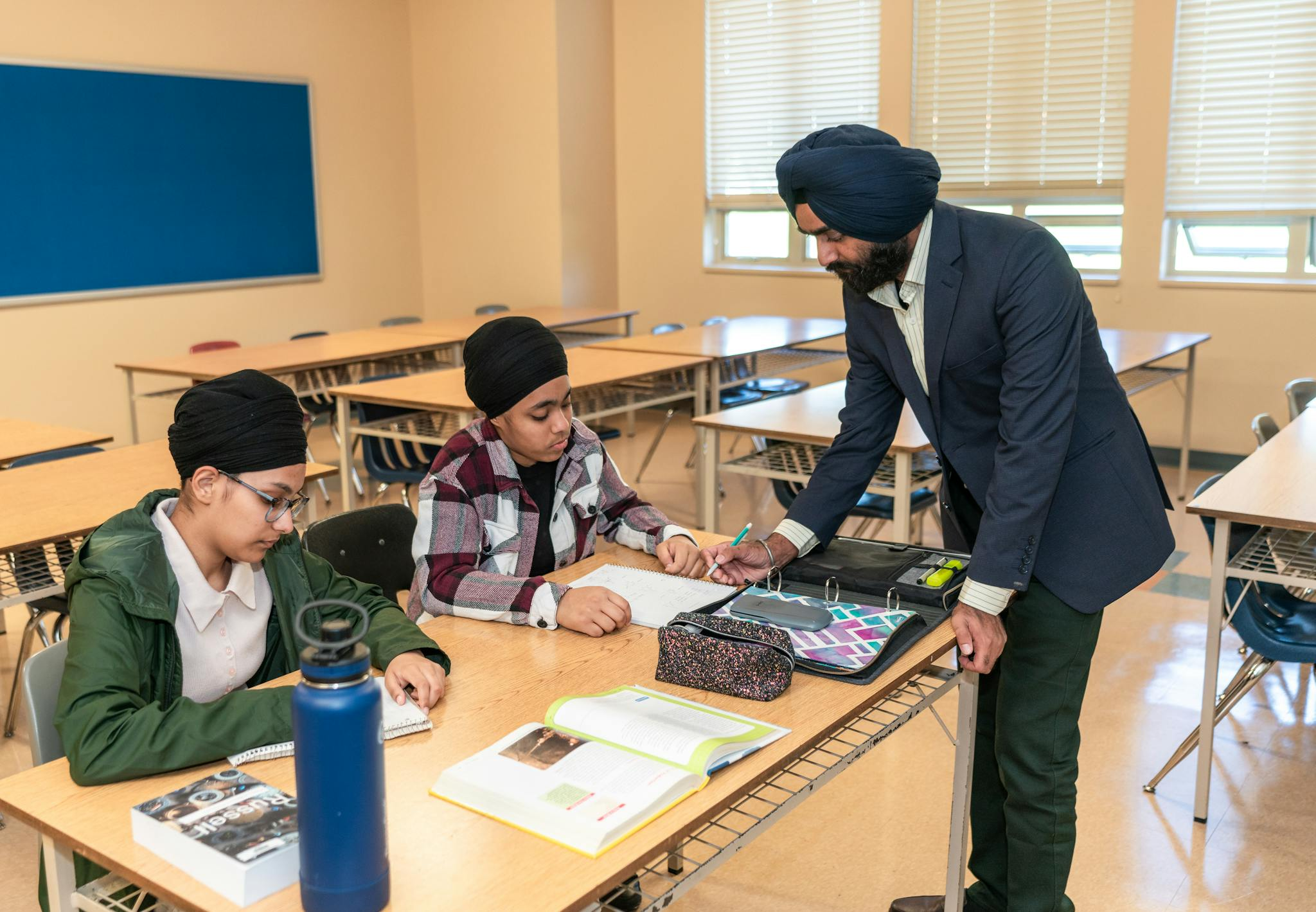 A teacher helps two students with homework in a bright classroom environment.